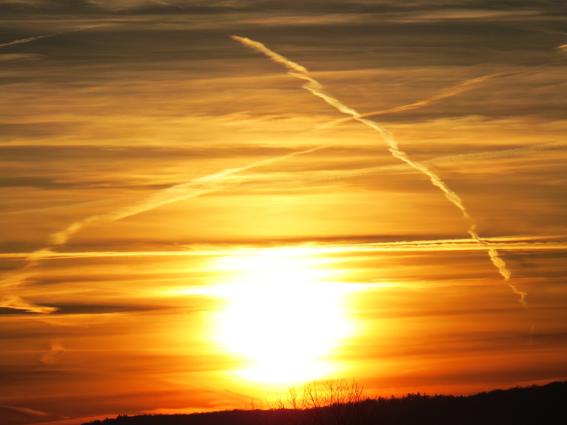 Airplane contrails flank a setting Sun. Credit: Hans/pixabay