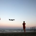 FILE PHOTO: Tourists take pictures on a beach while an airplane prepares to land in Cyprus October 22, 2017. Credit: Reuters/Yiannis Kourtoglou/File Photo