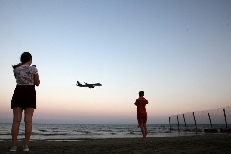 FILE PHOTO: Tourists take pictures on a beach while an airplane prepares to land in Cyprus October 22, 2017. Credit: Reuters/Yiannis Kourtoglou/File Photo