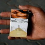 A man holds a pack of Marlboro cigarettes, which is the brand of Philip Morris, displaying health warning at a kiosk along a road in Karachi