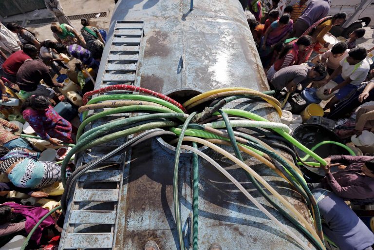 Residents with their empty containers crowd around a municipal tanker to fetch water in New Delhi