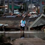 A local resident walks in front of submerged and destroyed houses in a flooded area in Kurashiki