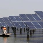 File photo of employees rowing a boat as they examine solar panel boards at a pond in Lianyungang