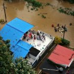 People wait for aid on the roof of their house at a flooded area in the southern state of Kerala