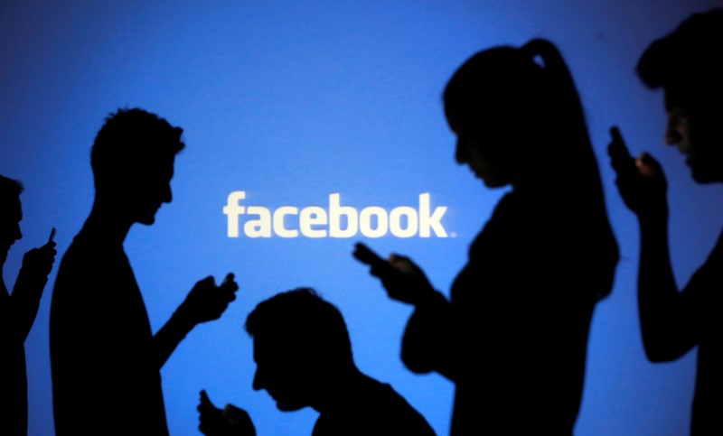 People are silhouetted as they pose with mobile devices in front of a screen projected with a Facebook logo, in this picture illustration October 29, 2014. Credits: Reuters /Dado Ruvic/Illustration/Files