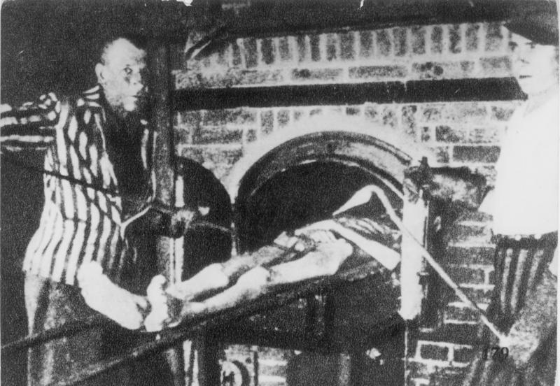 Survivors of KZ Dachau demonstrate the operation of the crematorium by pushing a corpse into one of the ovens. Credit: Wikipedia Commons