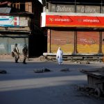 Indian security force personnel patrol past a Kashmiri woman in a deserted street during restrictions after scrapping of the special constitutional status for Kashmir by the Indian government, in Srinagar