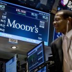 A screen displays Moody's ticker information as traders work on the floor of the New York Stock Exchange