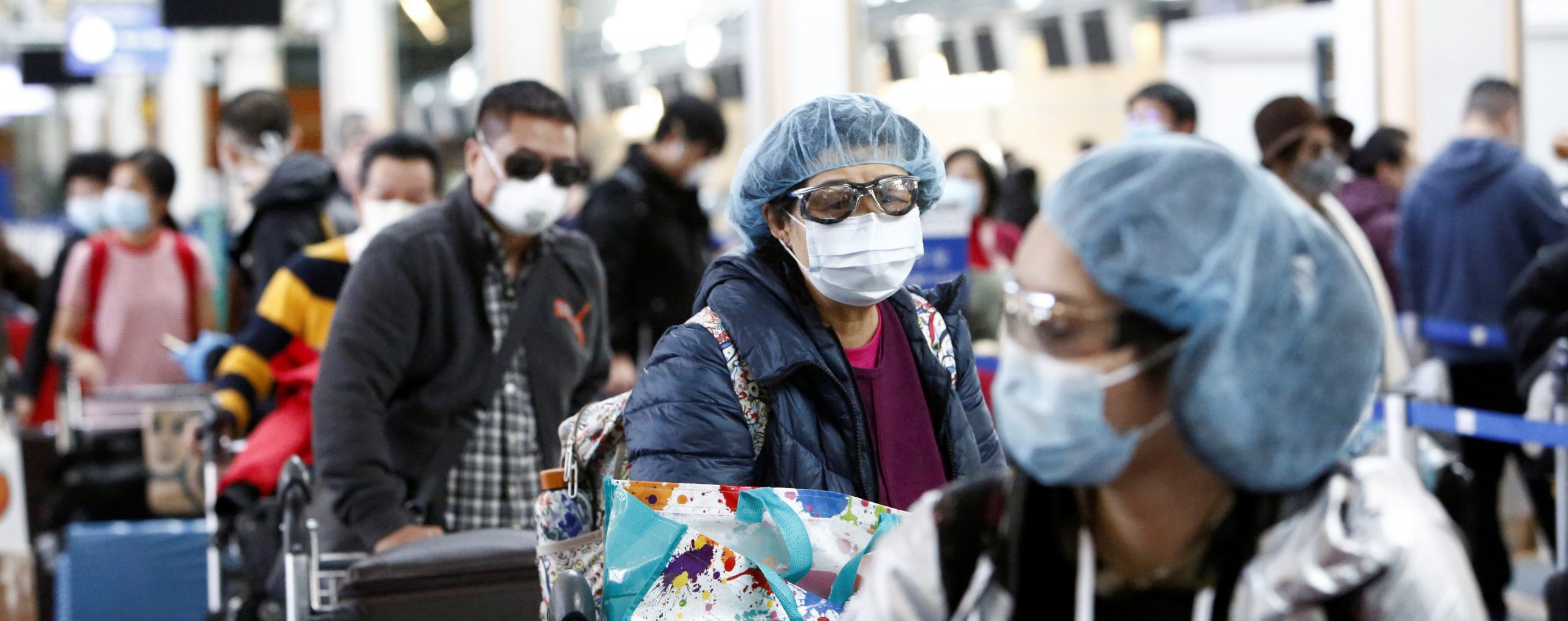 People wearing face masks and goggles wait to check in for an international flight at the Vancouver International Airport