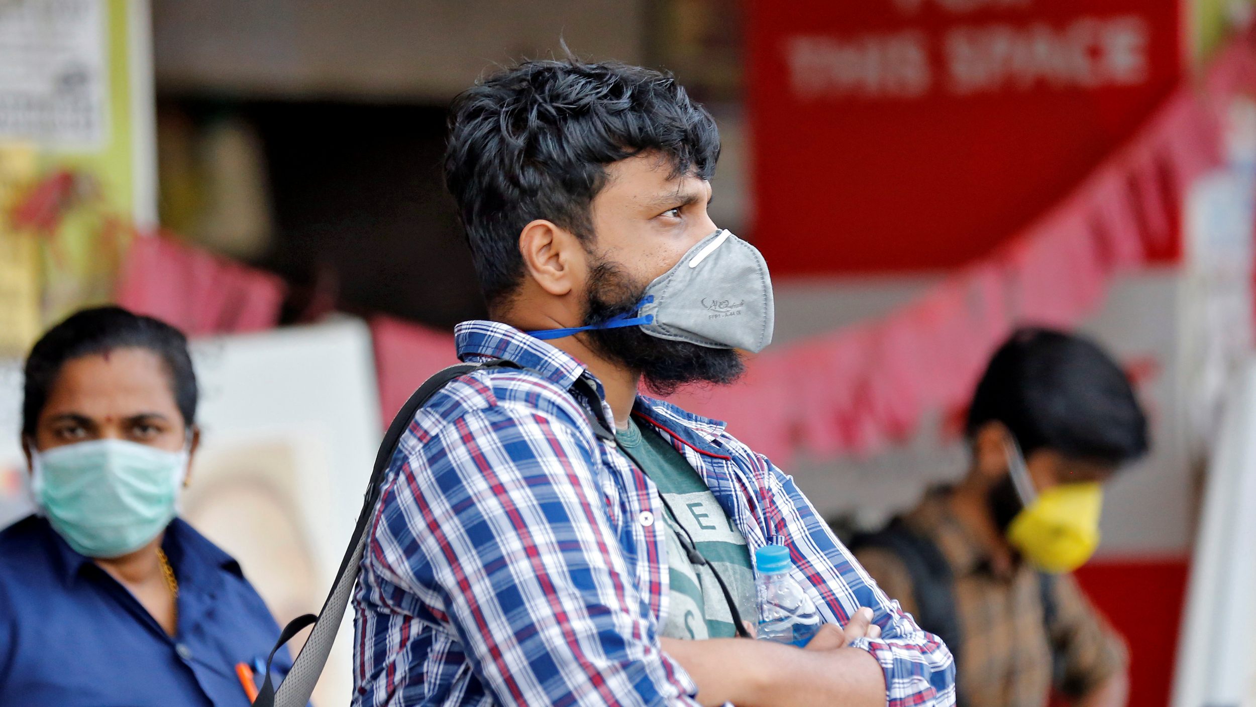 People wearing protective masks wait to board a bus at a terminal amid coronavirus fears, in Kochi