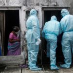 A woman watches as healthcare workers check the temperature of residents of a slum, in Mumbai