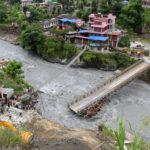 People gather near the bridge that is damaged due to the flood at Raghu Ganga River in Myagdi