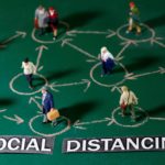 Small toy figures are placed on a chalkboard near "Social distancing" printed words in this illustration