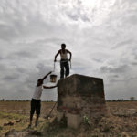 Farmers are pictured under monsoon clouds as they clean a canal water tank at Shantipura village in Gujarat