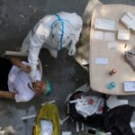 A health worker wearing personal protective equipment (PPE) collects a swab sample from a man in New Delhi