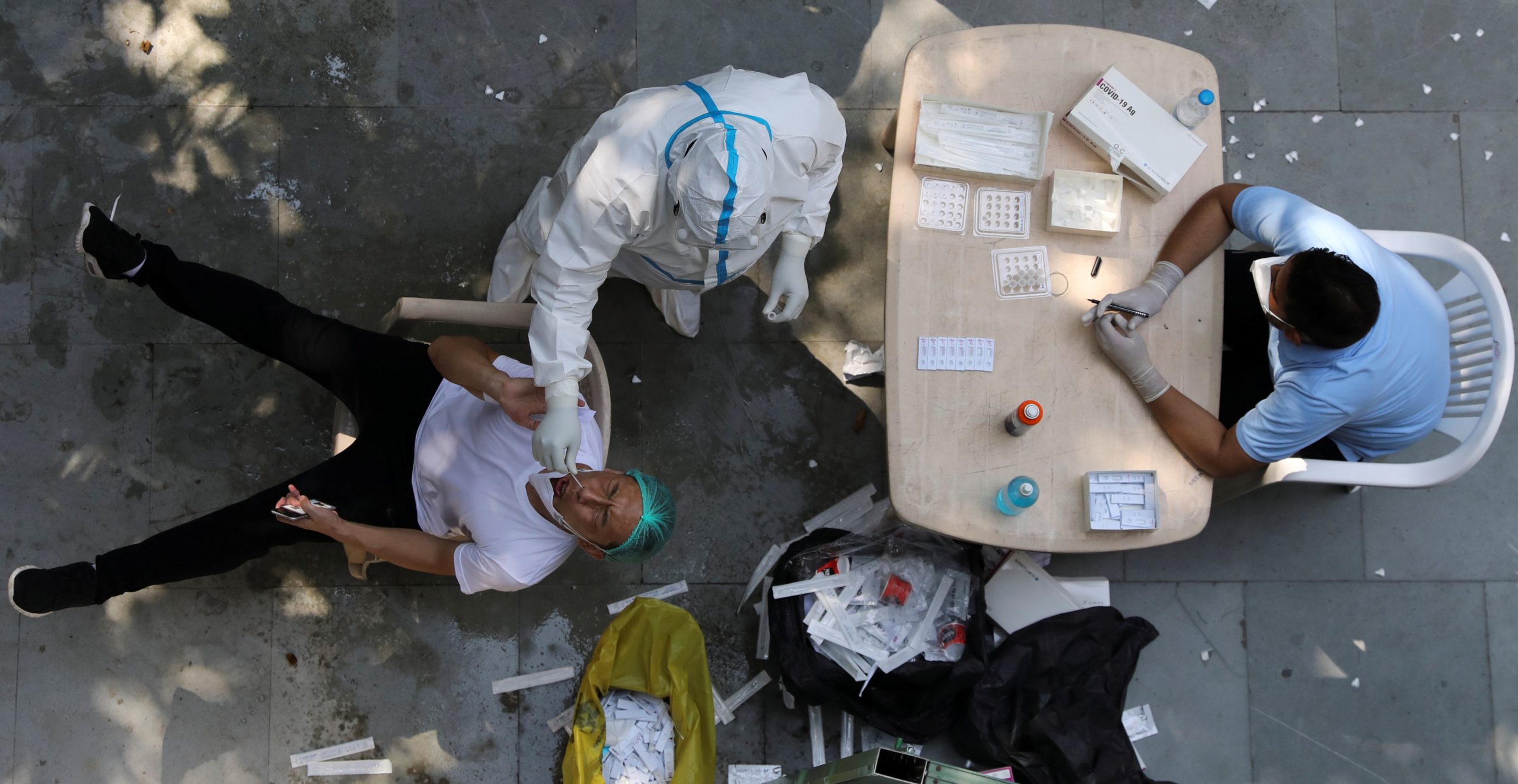 A health worker wearing personal protective equipment (PPE) collects a swab sample from a man in New Delhi