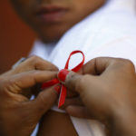 A red ribbon is put on the sleeves of a man by his friend to show support for people living with HIV during a program to raise awareness about AIDS on World AIDS Day in Kathmandu