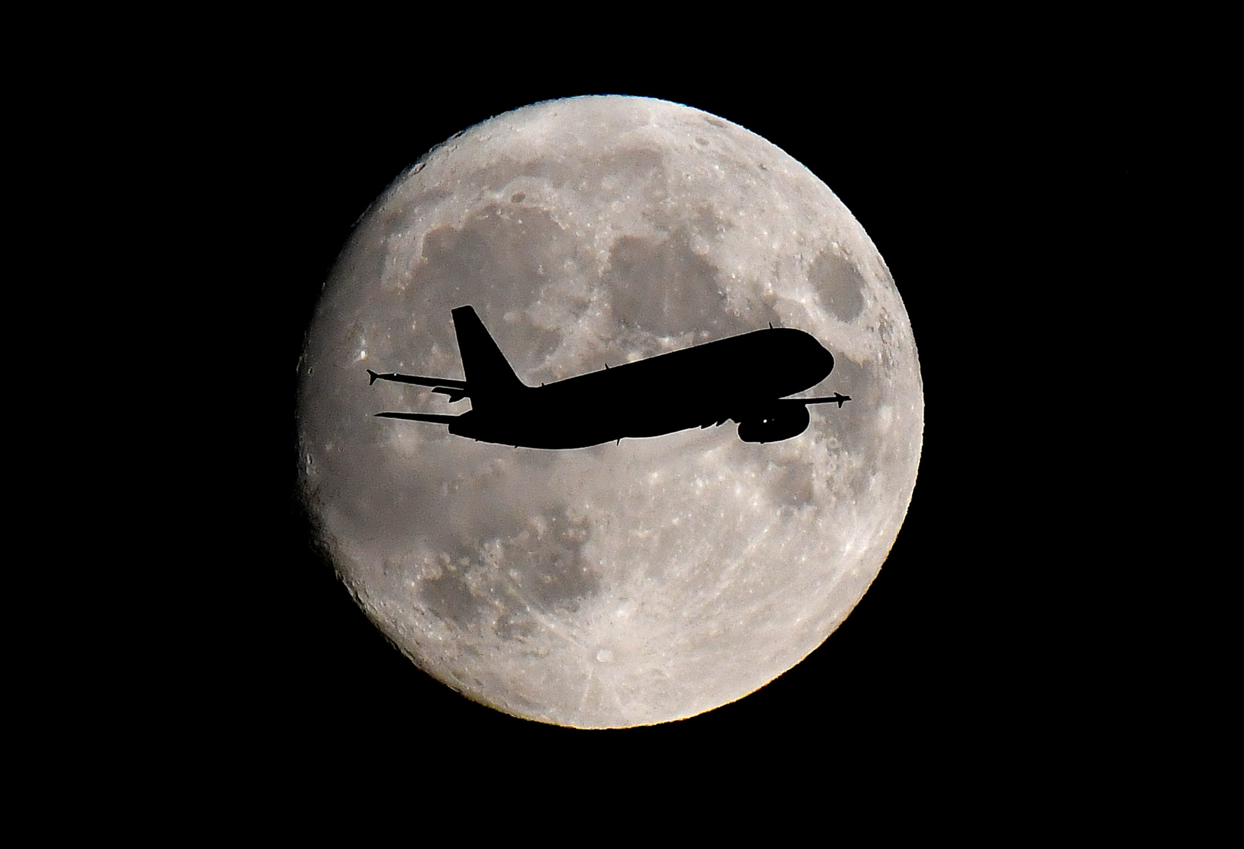 otA passenger plane passes in front of the moon as it makes its final landing approach to Heathrow Airport in London
