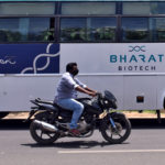 FILE PHOTO: A man rides his motorcycle past a parked bus of Indian biotechnology company Bharat Biotech outside its office in Hyderabad