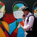 A man walks past a graffiti of people wearing protective masks amidst the spread of the coronavirus disease (COVID-19) on a street in Navi Mumbai