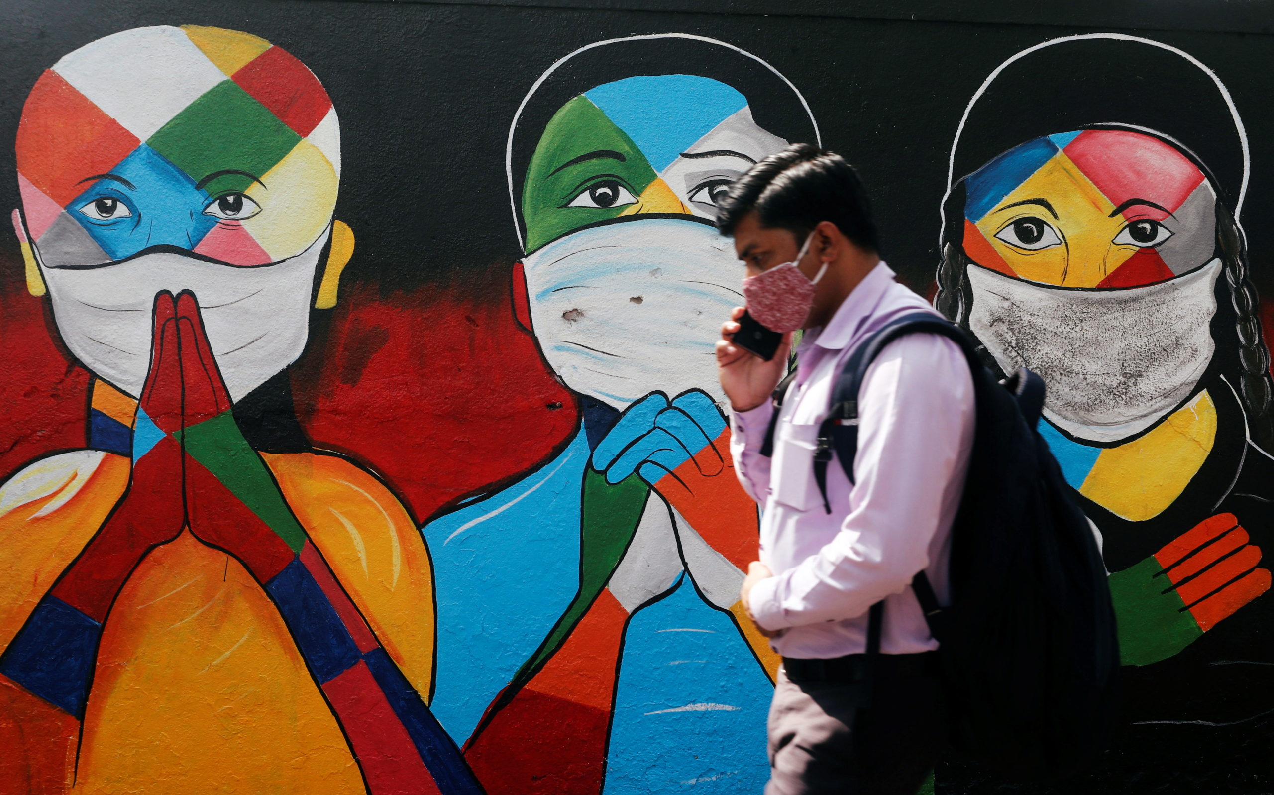 A man walks past a graffiti of people wearing protective masks amidst the spread of the coronavirus disease (COVID-19) on a street in Navi Mumbai
