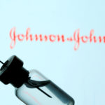Vial and syringe are seen in front of displayed Johnson&Johnson logo in this illustration