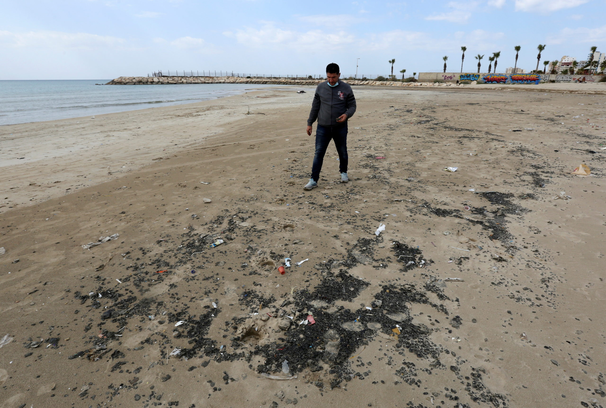 A man walks along a beach in the aftermath of an oil spill that drenched much of the Mediterranean shoreline, in Tyre nature reserve