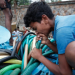 A boy uses his mouth to pump out water from a municipal tanker to fill his containers in New Delhi, India.