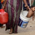 A woman carries her son in a bucket after collecting water from a municipal water tanker on the outskirts of Chennai, July 4, 2019. Photo: Reuters/P. Ravikumar