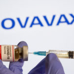 FILE PHOTO: A woman holds a small bottle labeled with a "Coronavirus COVID-19 Vaccine" sticker and a medical syringe in front of displayed Novavax logo in this illustration
