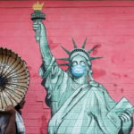 Man carrying a basket walks past a graffiti depicting the Statue of Liberty wearing a mask amidst the spread of the coronavirus disease, in Mumbai