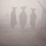 Kashmiri women carry baskets on their heads as they walk along the road amid dense fog on a cold morning in Srinagar