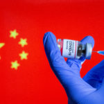 FILE PHOTO: A woman holds a small bottle labeled with a "Coronavirus COVID-19 Vaccine" sticker and a medical syringe in front of displayed China flag in this illustration