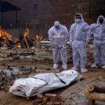 Men wearing protective suits stand next to the body of their relative, who died from the coronavirus disease (COVID-19), before her cremation at a crematorium ground in New Delhi