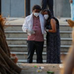A couple mourns as they stand next to the funeral pyre of a relative who died due to the coronavirus disease (COVID-19), at a crematorium in New Delhi