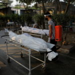 A municipal worker sprays disinfectant on the bodies of victims who died due to the coronavirus disease (COVID-19), at a crematorium in New Delhi