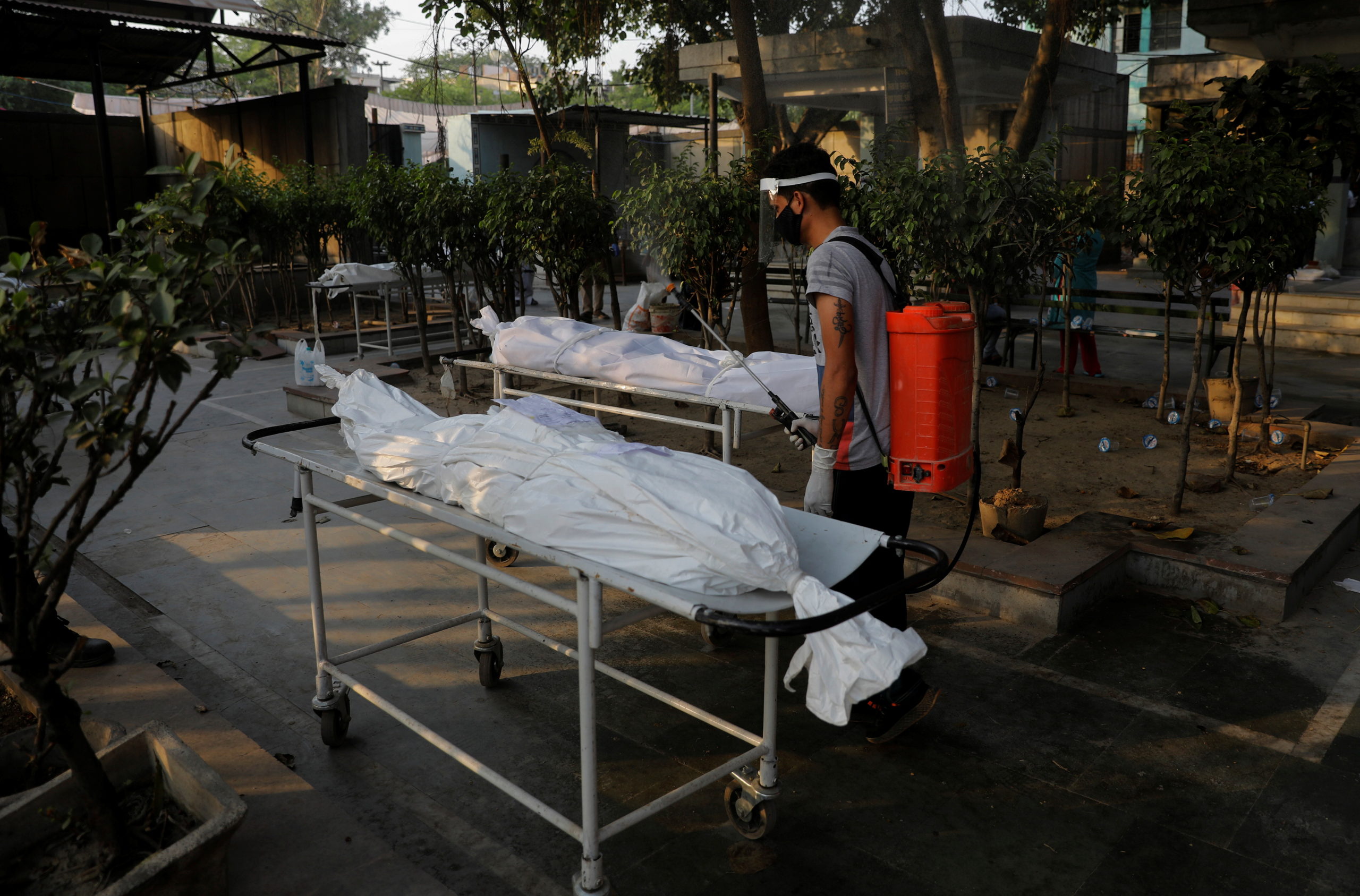 A municipal worker sprays disinfectant on the bodies of victims who died due to the coronavirus disease (COVID-19), at a crematorium in New Delhi