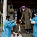A healthcare worker takes a nasal swab sample from a man for a coronavirus disease (COVID-19) test in front of a shop in Nawroz Baba village