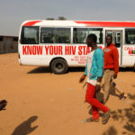 People walk past a bus during an HIV/AIDS awareness campaign on the occasion of World AIDS Day at the Kuchingoro IDPs camp in Abuja