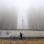FILE PHOTO: Woman wearing a mask walks past buildings on a polluted day in Hebei