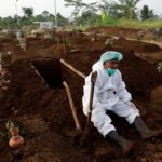 FILE PHOTO: A gravedigger wearing personal protective equipment rests in Indonesia