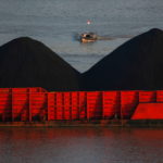 Man stands on a boat as coal barges queue to be pull along Mahakam river in Samarinda