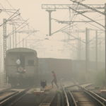 A woman crosses railway tracks as a goods train passes by, on a smoggy day in New Delhi