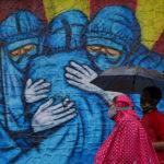 A woman and her son walk past a graffiti on a street, amidst the coronavirus disease (COVID-19) pandemic, in Mumbai