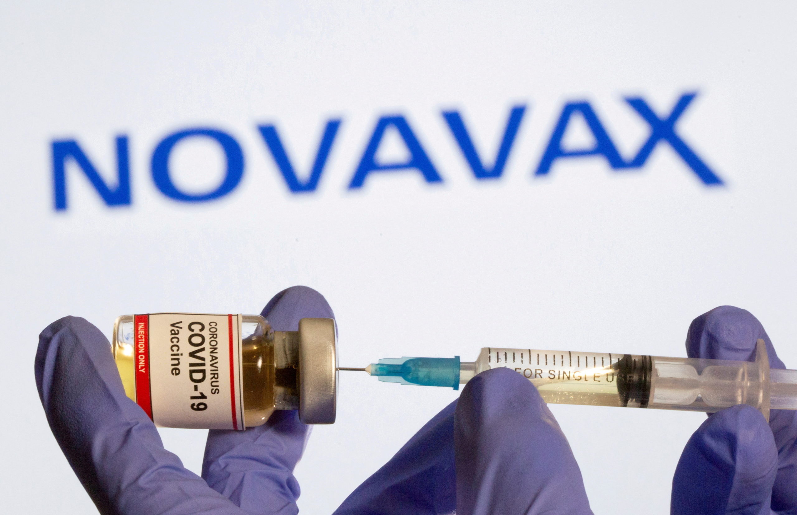 FILE PHOTO: FILE PHOTO: A woman holds a small bottle labeled with a "Coronavirus COVID-19 Vaccine" sticker and a medical syringe in front of displayed Novavax logo in this illustration