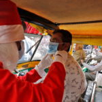 FILE PHOTO: A man wearing a Santa Claus costume helps an auto rickshaw driver to wear a protective face mask, in Ahmedabad