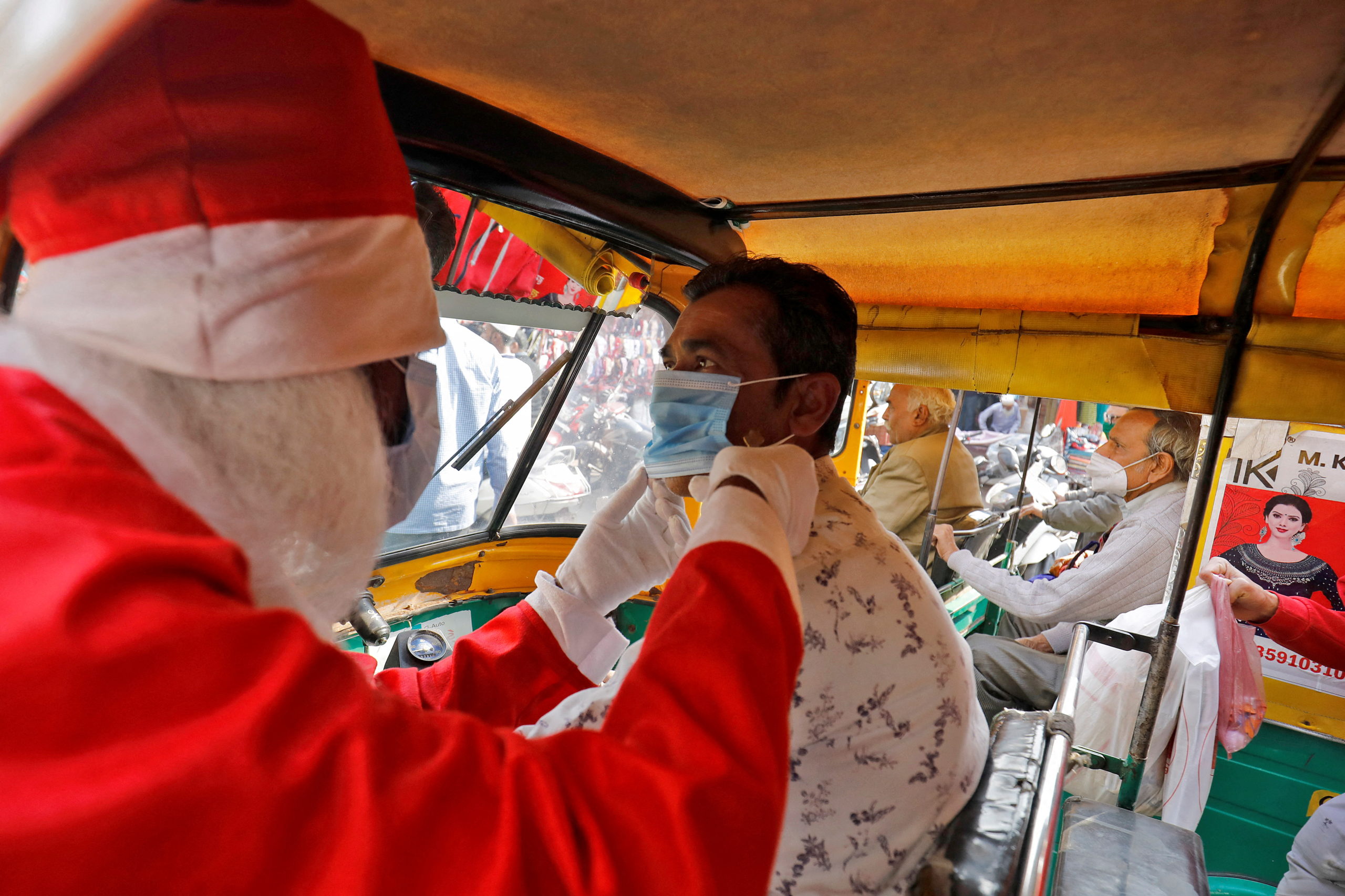 FILE PHOTO: A man wearing a Santa Claus costume helps an auto rickshaw driver to wear a protective face mask, in Ahmedabad