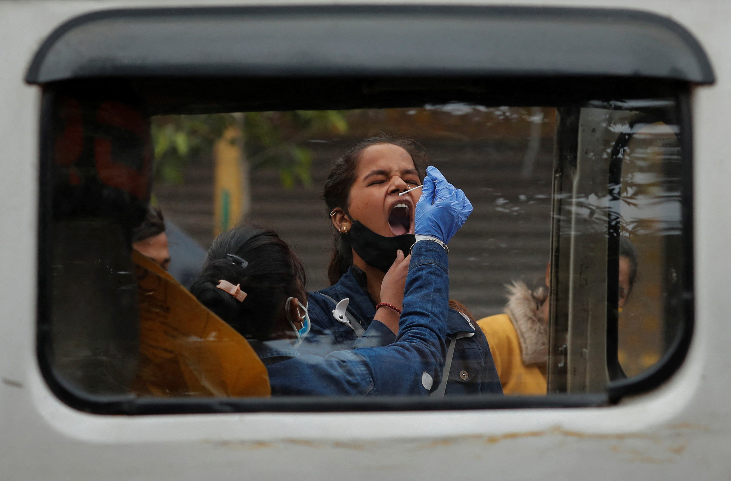 Healthcare worker collects COVID-19 test swab samples from people at a market area in Delhi
