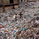 FILE PHOTO: Children walk over a polluted area as they collect plastic materials in Dhaka