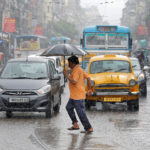 A man carrying an umbrella runs as he crosses a busy road during heavy rains in Kolkata